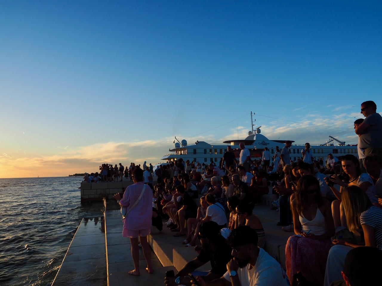 Menschen sitzen bei Sonnenuntergang an der Meeresorgel von Zadar.