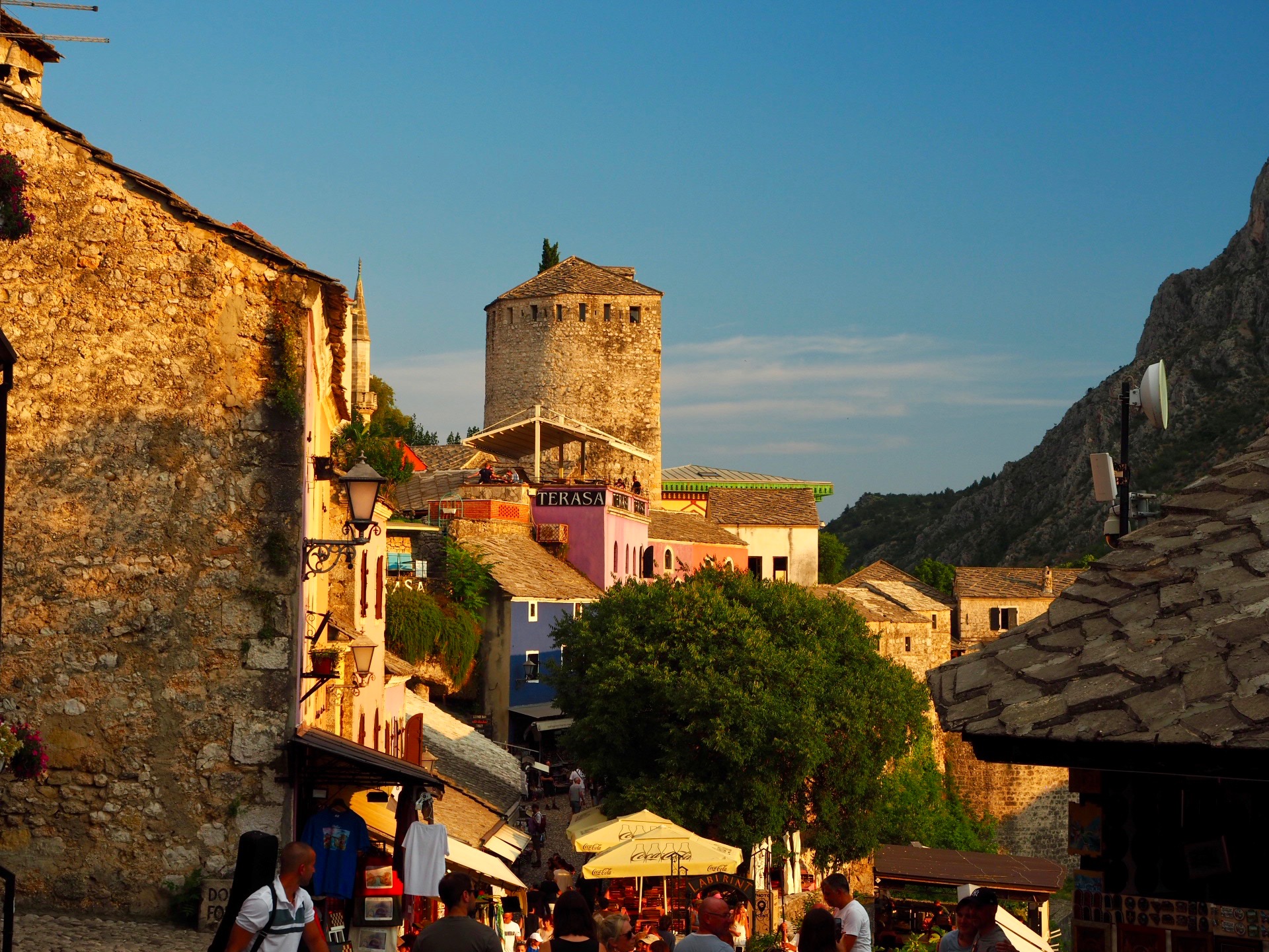 Mostar mit Stadtszene, Turm und Menschen im Abendlicht.